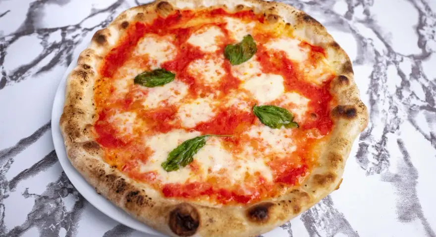 Pizza Margherita z pomidorami, mozzarellą i bazylią na białym talerzu na marmurowym tle.