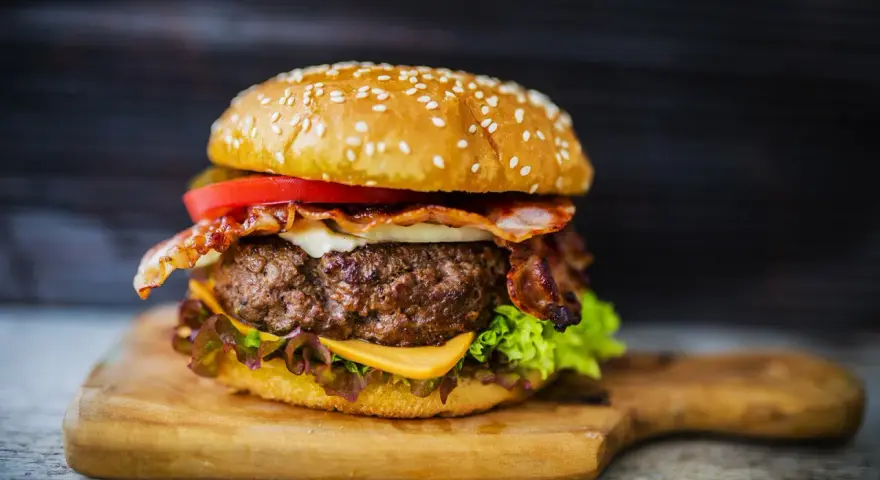 Soczysty hamburger z bekonem, serem, pomidorem i sałatą na desce.