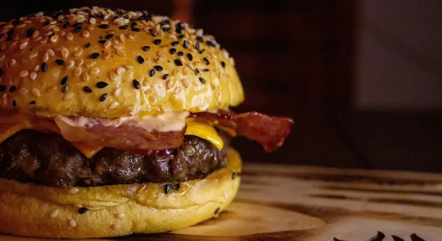 Soczysty domowy burger z bekonem i serem na bułce z sezamem.