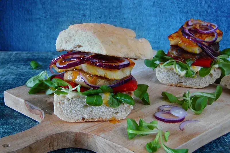 różne składniki na burgera, deska do krojenia, świeże warzywa, mięso, ser, bułka