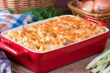 Zapiekanka makaronowa z kurczakiem w czerwonym naczyniu, posypana roztopionym serem.