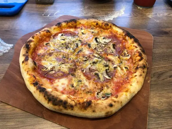 Domowa pizza z pieczarkami i salami na drewnianej desce.