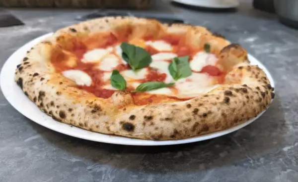 Pizza Margherita na białym talerzu, z widocznym puszystym brzegiem i świeżą bazylią.